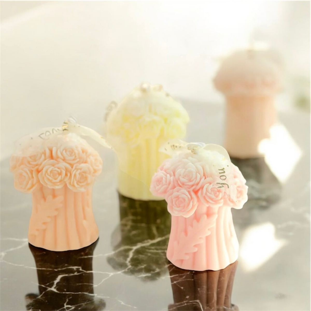 Rose bouquet scented candles in peach, yellow and pink on a marble surface