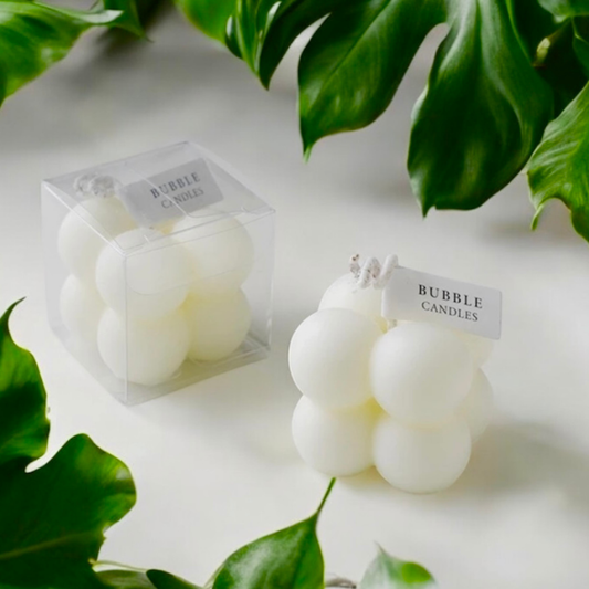 White bubble cube scented candle with its clear gift box among green leaves