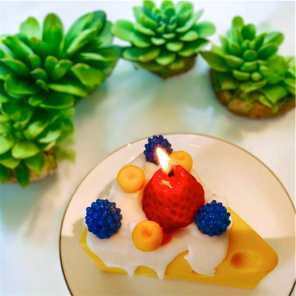 Lit cheese wedge scented candle with strawberry and berries on a plate with succulents