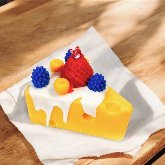 Cheese wedge scented candle topped with strawberry and blueberries on a white napkin
