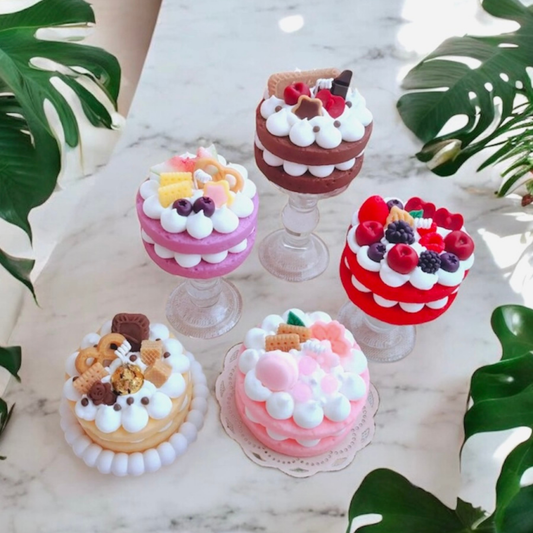 Five two layer mini cake scented candles in purple, chocolate, red berry, cookie and pink on marble