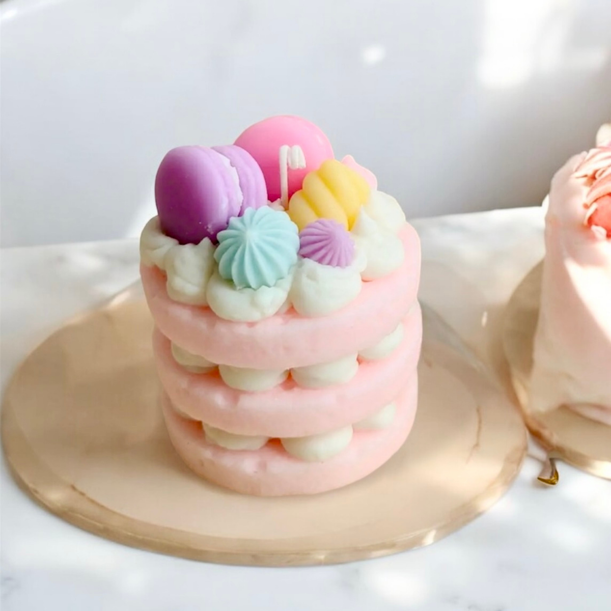 Pink three layer cake scented candle topped with pastel macarons on a gold tray