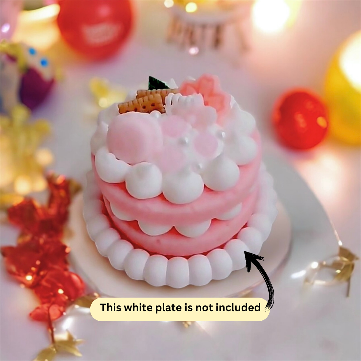 Pink two layer cake scented candle with pearl cream trim and party balloons behind