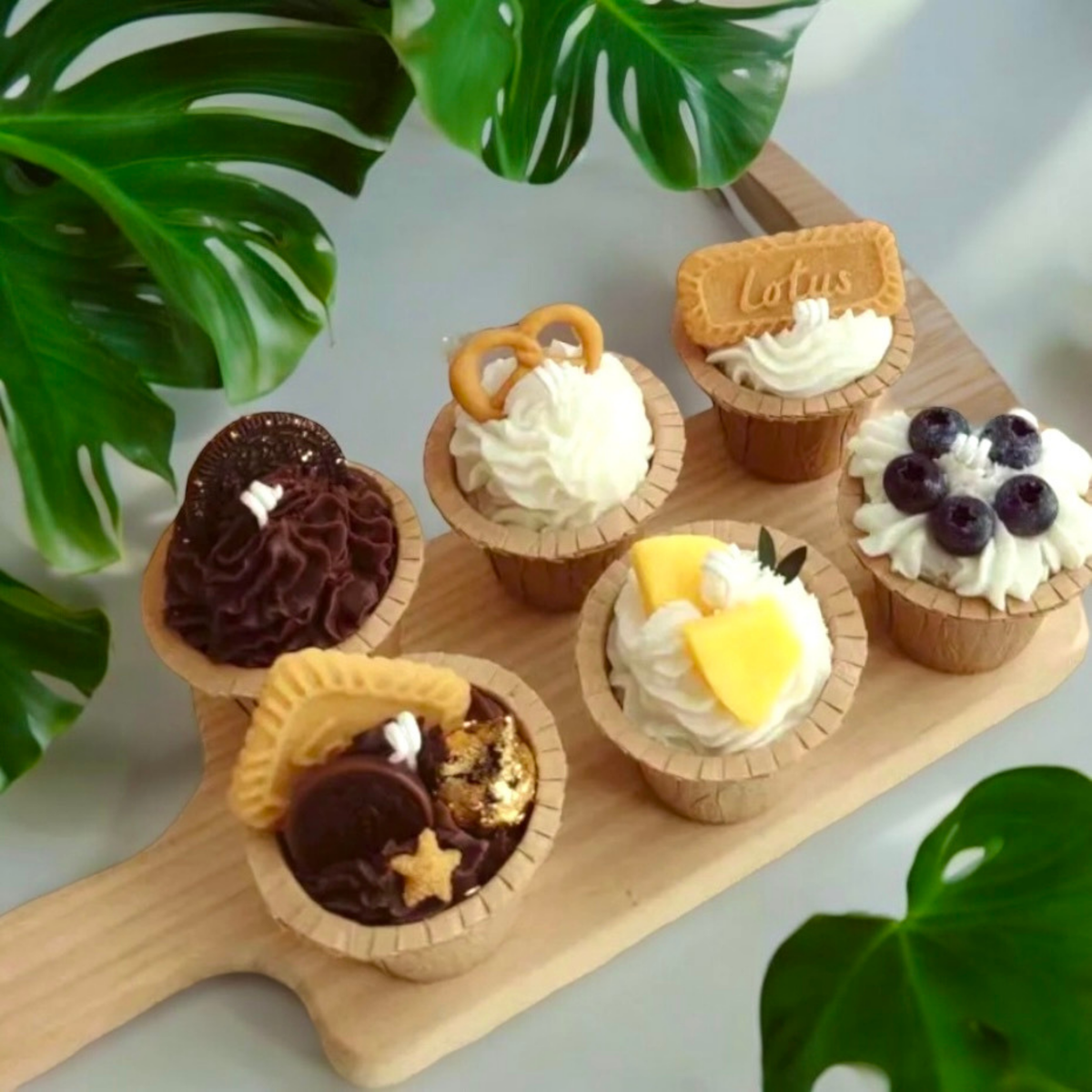 Seven mini cupcake scented candles on a wooden paddle with biscuit, blueberry and mango toppings
