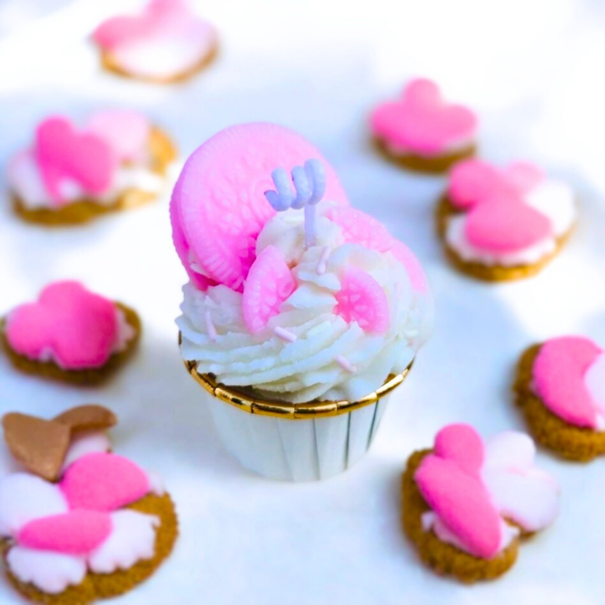 White frosted cupcake scented candle with a pink sandwich biscuit and heart cookies