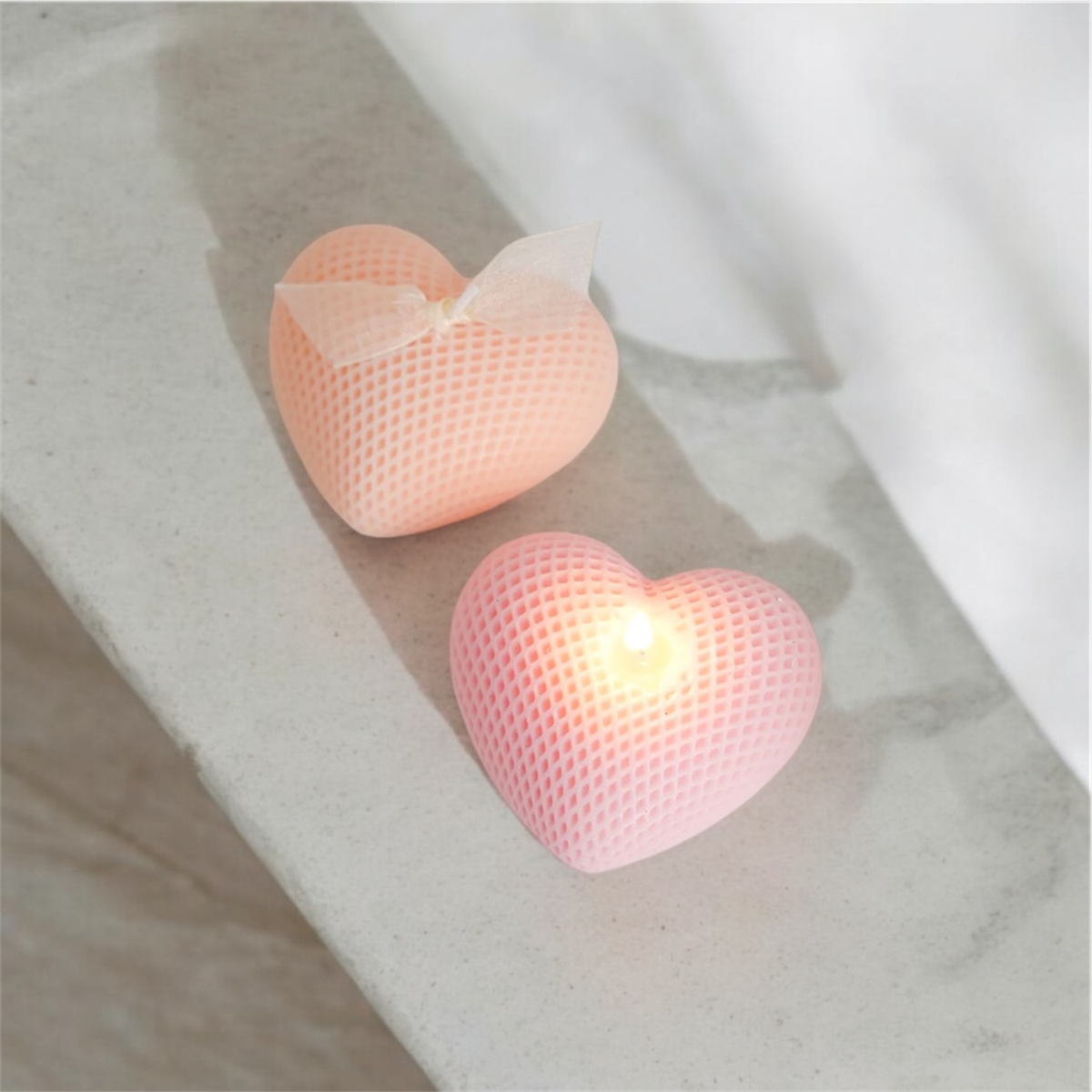 Peach and pink waffle textured heart scented candles, one lit, on a stone ledge