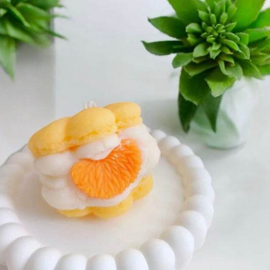 Yellow macaron scented candle with orange slice filling on a white dish