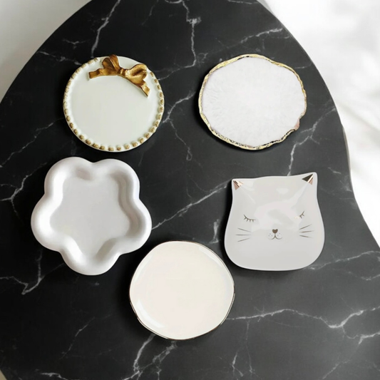 Five ceramic candle plates - gold bow, geode edge, flower, cat and round - on black marble