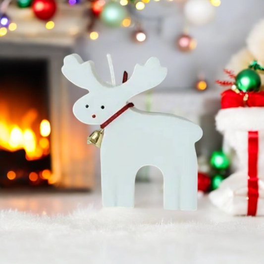 White reindeer shaped scented candle with red collar and gold bell by a fireplace