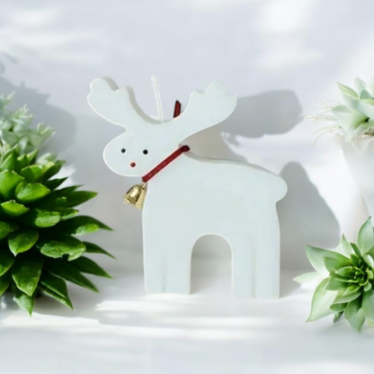 White reindeer shaped scented candle with gold bell beside green succulents