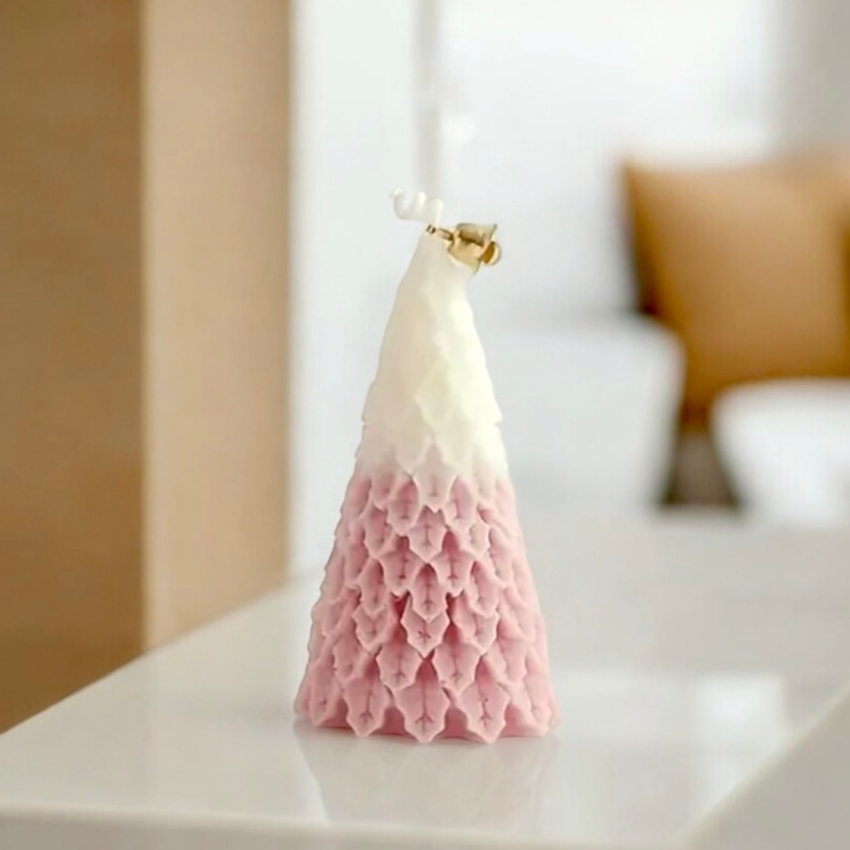 Pink ombre Christmas tree scented candle with gold bell on a white table