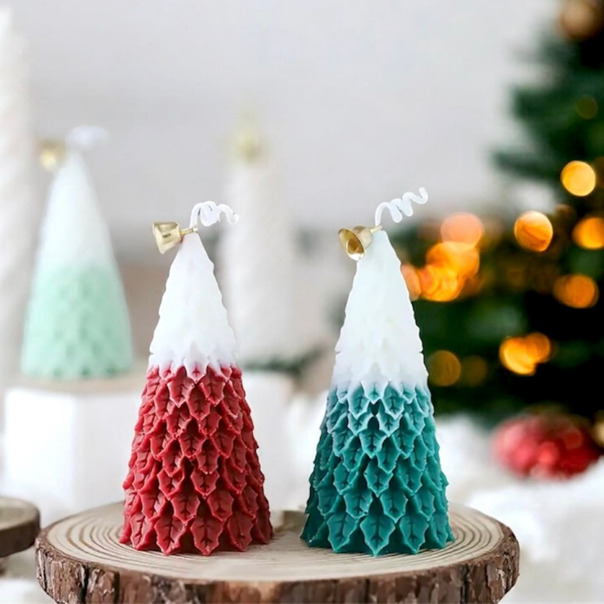 Red and teal ombre Christmas tree scented candles with gold bells on a wood slice